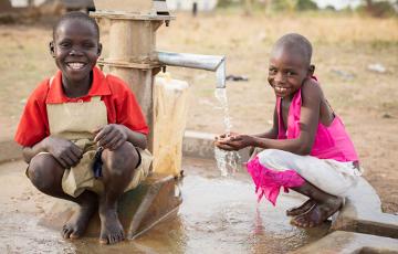 Zwei Kinder vor einem Brunnen in Uganda