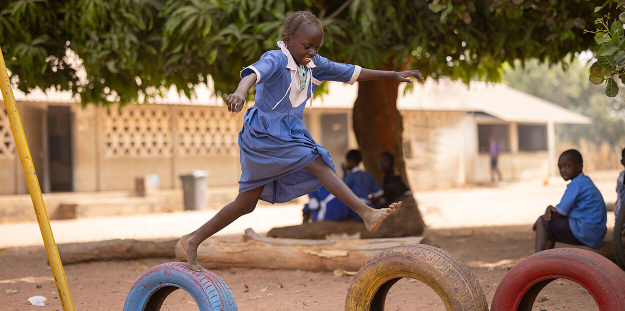 Ein Mädchen springt auf einem Schulhof über alte Autoreifen.