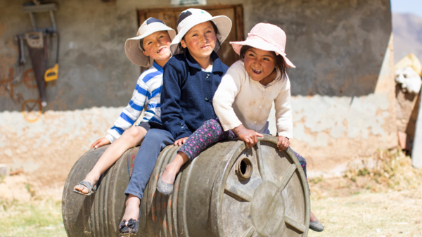 Drei bolivische Kinder sitzen auf einem Fass.