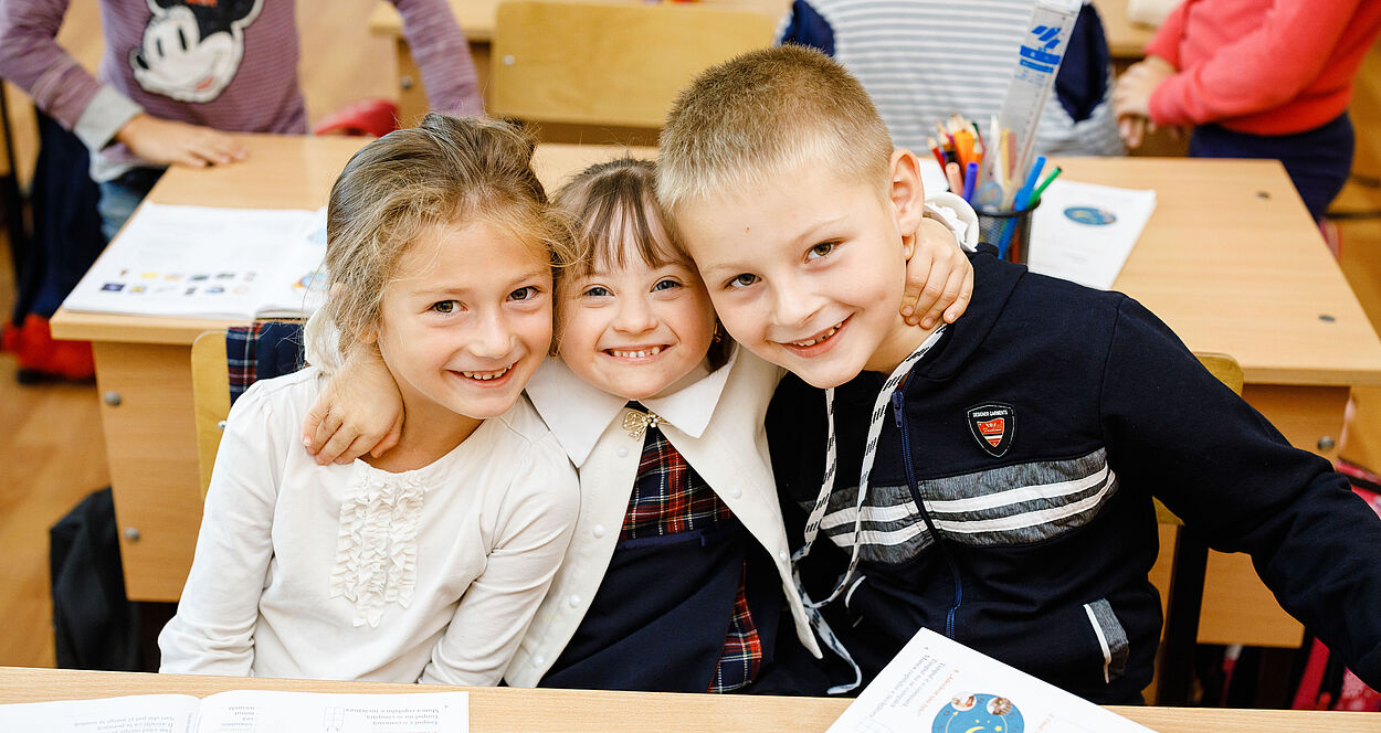 Drei Schulkinder sitzen an einem Pult.