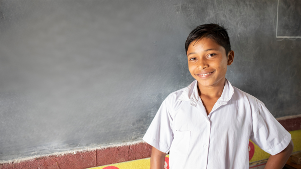 A boy is standing in front of a blackboard in the classroom.