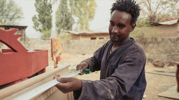 A young man is measuring a piece of wood.