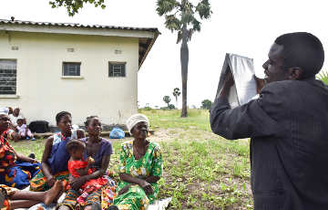 Eine Projektgemeinschaft in Sambia sitzt auf der Wiese und wird von einem Mitarbeiter aufgeklärt