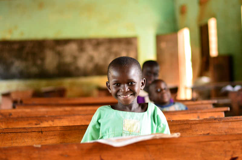 Kind sitzt in einem fast leeren Klassenraum in Uganda